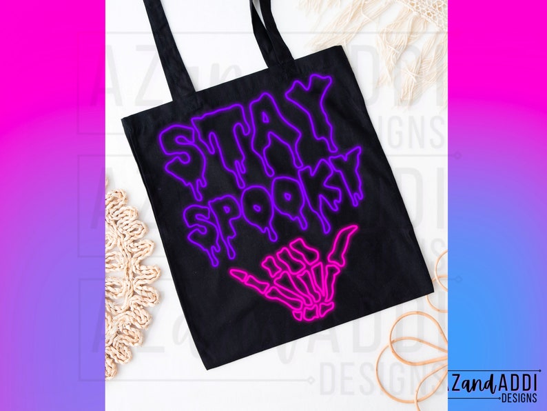 May include: Black tote bag with a neon pink and purple graphic that says "Stay Spooky" with a skeleton hand making a shaka sign.