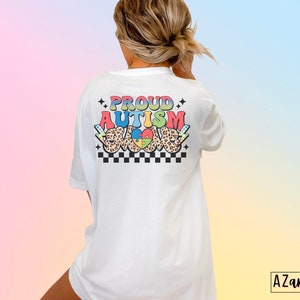 May include: White t-shirt with the text "PROUD AUTISM LOVE" in rainbow colors with a checkered pattern and a leopard print heart with a puzzle piece inside.