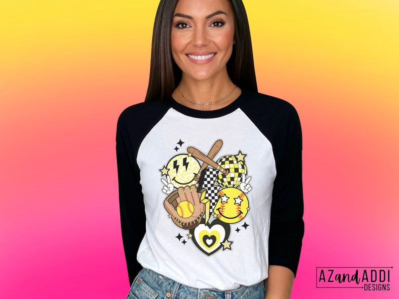 May include: White and black raglan baseball tee with a softball-themed graphic. The graphic includes smiley faces, a baseball glove, bats, and stars. The shirt has black sleeves and a white body. The text "AZandAddi Designs" is in the bottom right corner.