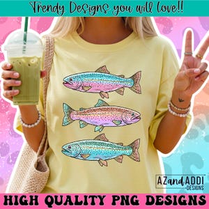 Puede incluir: Camiseta amarilla con tres ilustraciones de peces coloridos en tonos azules, rosas y marrones. La camiseta tiene el texto "Trendy Designs you will love!!" y "HIGH QUALITY PNG DESIGNS".