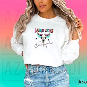 May include: White long-sleeved sweatshirt with a colourful graphic of a cow skull with the text "Long Live Cowgirls".