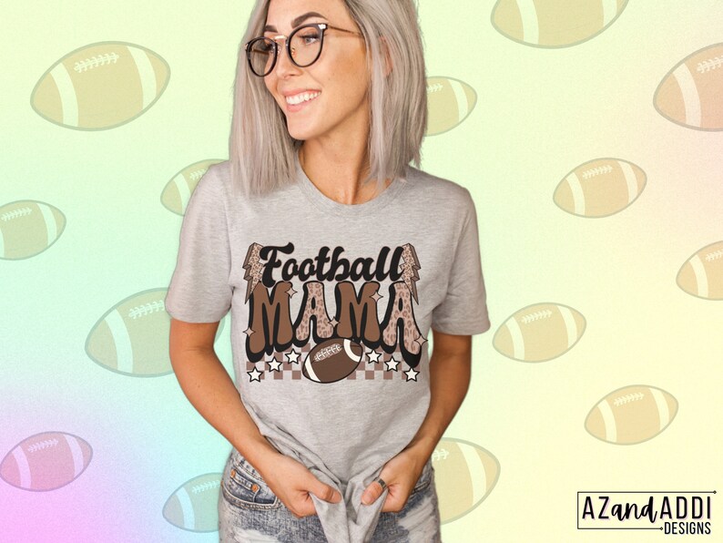 Pode incluir: Uma camiseta cinza com o texto "Football Mama" em letras marrons e pretas com um design de estampa de leopardo. O texto &eacute; cercado por estrelas e uma bola de futebol.