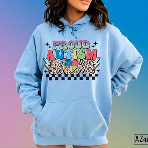 May include: A light blue hoodie with a graphic design that says "Proud Autism Love" in rainbow colors with a puzzle piece heart and leopard print accents.