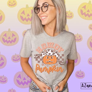 May include: A light gray t-shirt with the text "Howdy Pumpkin" in orange and peach colors. The design features a pumpkin wearing a cowboy hat and stars. The shirt is a Halloween-themed graphic tee.