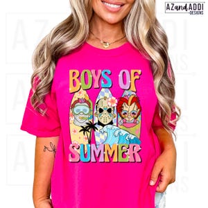 May include: A hot pink t-shirt with the words "BOYS OF SUMMER" in colorful, retro lettering. The graphic features three cartoon characters on surfboards, with a wave and palm trees. The shirt is a vibrant, eye-catching design.