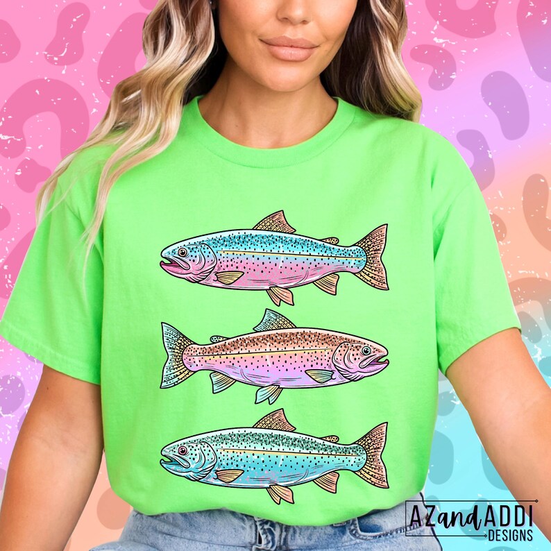 Puede incluir: Una camiseta verde lima con tres ilustraciones de peces coloridos. Cada pez tiene una combinaci&oacute;n de colores &uacute;nica, con tonos de azul, rosa y marr&oacute;n. La camiseta tiene el texto "AZandADDI DESIGNS" en la esquina inferior derecha.