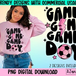 May include: A light pink sweatshirt with the words "GAME DAY" in a black, retro font, a pink lightning bolt, and a soccer ball graphic. The image also includes the text "TRENDY DESIGNS WITH COMMERCIAL USAGE" and "PNG DIGITAL DOWNLOAD".