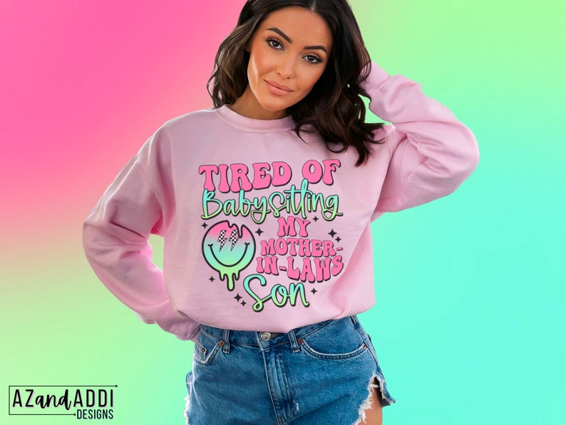 Puede incluir: Sudadera rosa con el texto "TIRED OF Babysitting MY MOTHER-IN-LAWS Son" en una fuente colorida y con goteo con un gr&aacute;fico de cara sonriente.