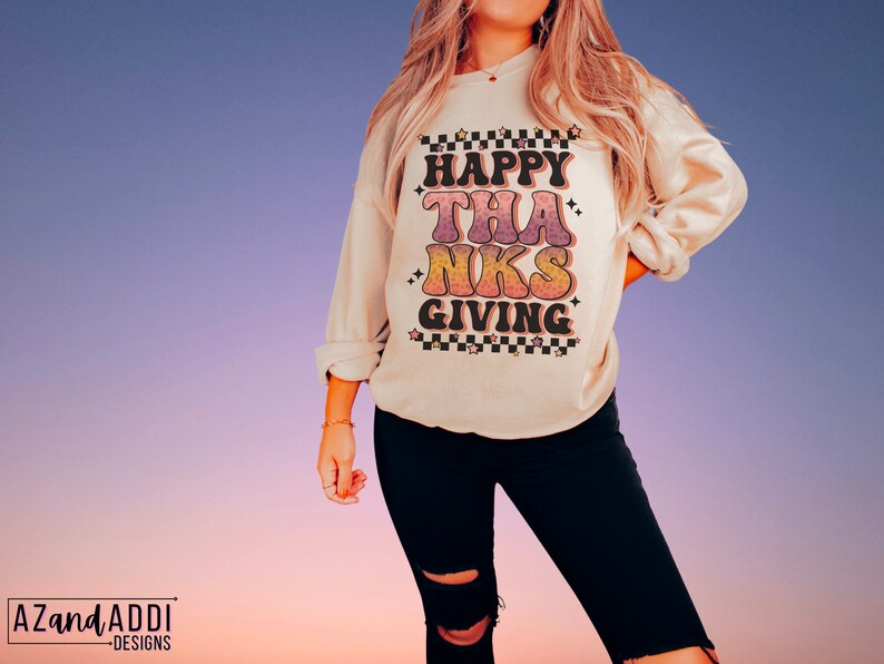May include: A cream colored sweatshirt with the text "HAPPY THANKSGIVING" in a retro font with colorful accents and black stars.
