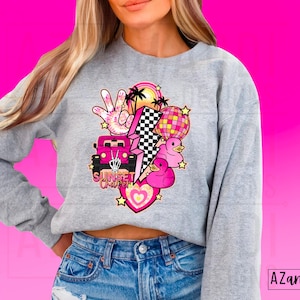 May include: Gray sweatshirt with a pink and white graphic design featuring a car, a lightning bolt, a peace sign, palm trees, a disco ball, and rubber ducks. The text "Sunset Chaser" is included in the design.