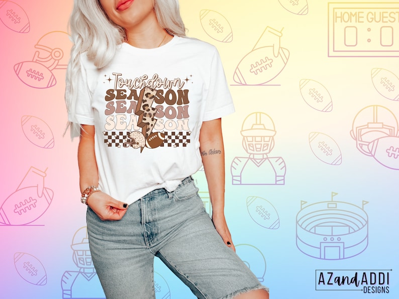 May include: White t-shirt with a brown, black, and white graphic that says "Touchdown Season" with a lightning bolt and footballs. The graphic has a checkered pattern and a leopard print.