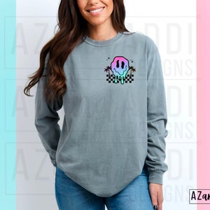 May include: A grey long-sleeved t-shirt with a colourful dripping smiley face graphic and palm trees on a chequered background.