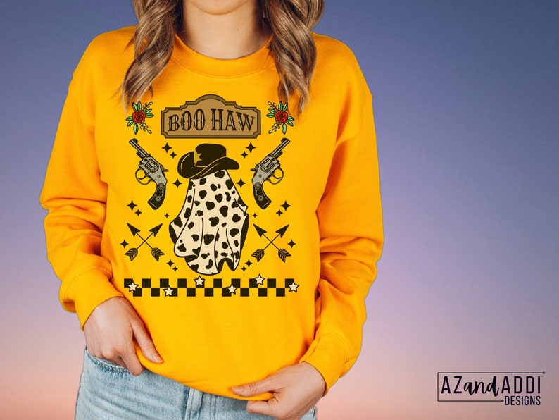 Puede incluir: Sudadera amarilla con un fantasma que lleva un sombrero de vaquero y sostiene dos pistolas. El texto "BOO HAW" est&aacute; en un cartel sobre el fantasma. La sudadera tiene un patr&oacute;n de cuadros en la parte inferior.