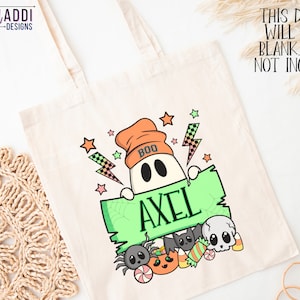 K&ouml;nnte beinhalten: Eine cremefarbene Tragetasche mit einem Halloween-Design. Sie zeigt einen Geist mit einer orangefarbenen M&uuml;tze, der ein gr&uuml;nes Schild mit dem Namen "AXEL" h&auml;lt. Das Design umfasst Sterne, Blitze und Halloween-Leckereien. Der Text auf der Tasche lautet "THIS DESIGN WILL COME BLANK. NAME NOT INCLUDED."