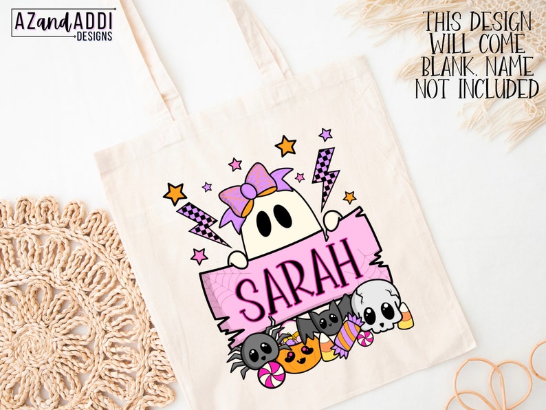 K&ouml;nnte beinhalten: Eine cremefarbene Tragetasche mit einem Halloween-Design. Das Design zeigt einen Geist, der ein rosa Schild mit dem Namen "SARAH" h&auml;lt, umgeben von Sternen, einer Spinne, S&uuml;&szlig;igkeiten und einer Fledermaus. Der Text "THIS DESIGN WILL COME BLANK. NAME NOT INCLUDED" ist ebenfalls sichtbar.