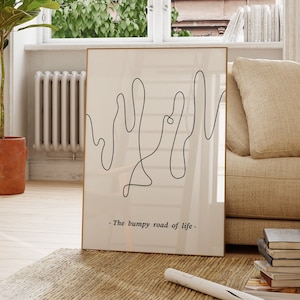 May include: A black and white line art print of a wavy line with the text "The bumpy road of life". The print is framed and hanging on a wall in a living room.