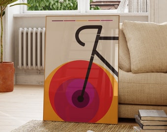May include: A minimalist poster with a black bicycle silhouette on a background of concentric circles in shades of red, orange, and purple. The poster is framed in gold and hanging on a white wall in a living room setting.