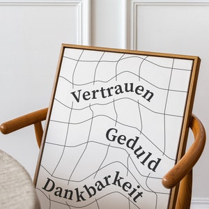 May include: A framed print with a white background and black grid pattern. The words "Vertrauen", "Geduld", and "Dankbarkeit" are written in black on the print.