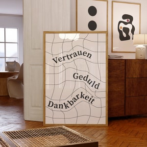 May include: A framed print with a white background and black grid pattern. The words "Vertrauen", "Geduld", and "Dankbarkeit" are written in black on the grid.