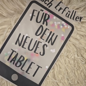 Könnte beinhalten: Eine tabletförmige Karte mit dem deutschen Text "Wunsch Erfüller FÜR DEIN NEUES TABLET" in Schwarz. Die Karte hat eine transparente Mitte, gefüllt mit bunten Konfetti, vor einem flauschigen, cremefarbenen Hintergrund.