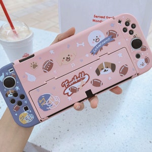 Op de afbeelding: Roze Nintendo Switch-hoes met verschillende stickers met hondenmotieven, waaronder pootjes, voetballen en de tekst "Championship" en "Football".