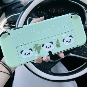 以下が含まれることがあります： パンダと竹のデザインが施された薄い緑色のニンテンドースイッチケース。ケースには「Sleepy Forest」の文字が印刷されています。