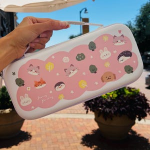 Puede incluir: Estuche de transporte blanco y rosa con asa, decorado con animales y árboles de dibujos animados. El estuche tiene cierre de cremallera y un asa blanca. El diseño incluye gatos, conejos, un perro y un erizo. El texto "Starry Forever" está impreso en el estuche.