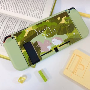 May include: A green and brown Nintendo Switch case with a starry forest design. The case features a squirrel and a hedgehog in a leafy setting. The text "Starry Forest" is printed on the case.