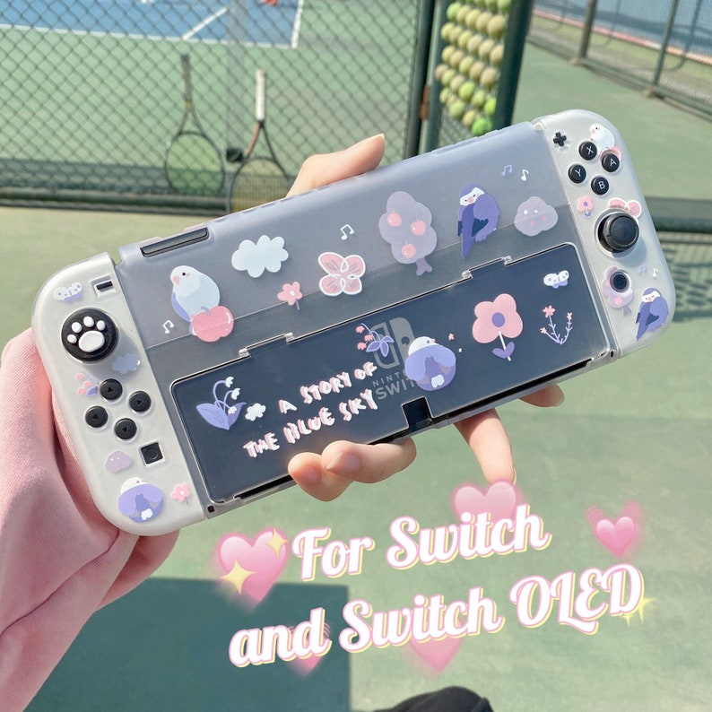 K&ouml;nnte beinhalten: Eine transparente Switch- und Switch OLED-H&uuml;lle, verziert mit Aufklebern von V&ouml;geln, Blumen und Wolken. Die H&uuml;lle tr&auml;gt den Text "A Story of the Blue Sky" und wird vor einem gr&uuml;nen Hintergrund gehalten.