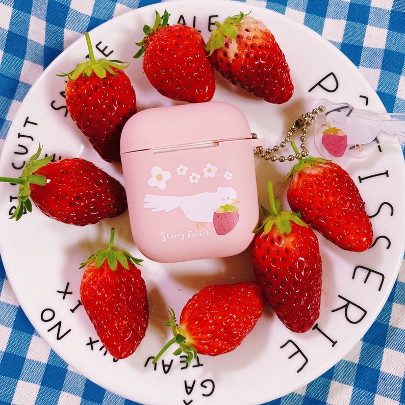 Puede incluir: Una funda rosa para Airpods con un dise&ntilde;o de p&aacute;jaro blanco y flores. La funda tiene el texto "Starry Forest". La funda est&aacute; rodeada de fresas rojas en un plato blanco con texto negro.