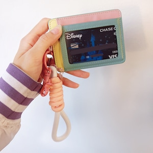 May include: A pastel pink, yellow, and green card holder with a white lanyard. The card holder has a clear plastic window to display a credit card with the text "Disney" and "CHASE" on it.