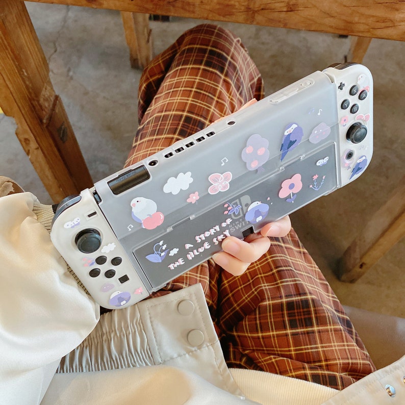 K&ouml;nnte beinhalten: Eine graue Nintendo Switch-Konsole mit einer transparenten Schutzh&uuml;lle. Die H&uuml;lle ist mit Cartoon-V&ouml;geln, Blumen und Wolken verziert. Der Text "A Story of the Blue Sky" ist auf der H&uuml;lle aufgedruckt.