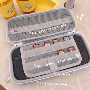 May include: A gray, zippered carrying case for a gaming console, open to reveal the console and game cartridges. The case has a soft velvet lining, a secure strap, and slots for 10 game cards. The text "Accessories pocket", "10 Game Cards Slots", "Secure strap", and "Soft velvet lining" are visible.