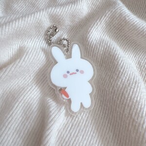 Op de afbeelding: Een witte konijnen sleutelhanger met een wortel in zijn hand. De sleutelhanger is gemaakt van helder acryl en heeft een zilveren ketting.