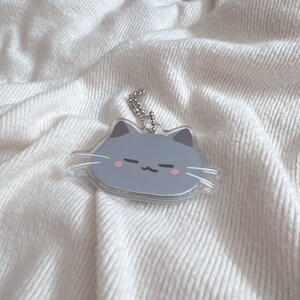 Op de afbeelding: Een grijze kattenhanger met roze wangen en witte snorharen. De hanger is bevestigd aan een zilveren ketting.