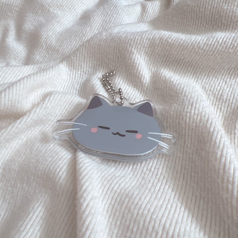 Op de afbeelding: Een grijze kattenhanger met roze wangen en witte snorharen. De hanger is bevestigd aan een zilveren ketting.