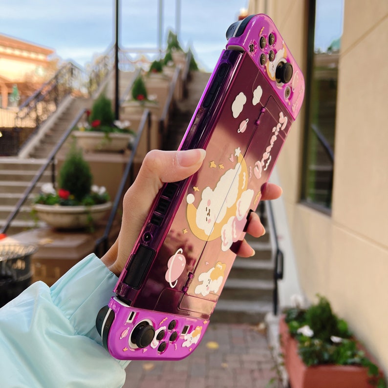 May include: A purple Nintendo Switch case with a cute cartoon character design. The case features a white cloud with a sleeping character, stars, and the word "Dreaming".