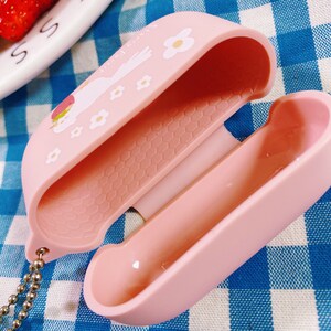 Puede incluir: Una funda de silicona rosa con un dise&ntilde;o floral y un gr&aacute;fico de fresa. La funda est&aacute; abierta para revelar un interior rosa suave. La funda tiene un peque&ntilde;o lazo de metal para sujetar un llavero.