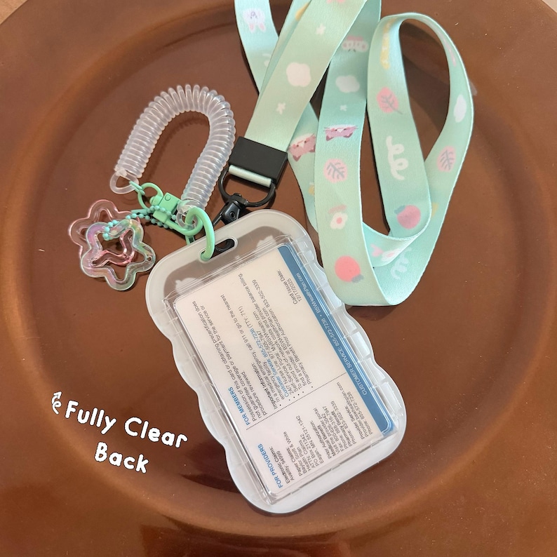 Op de afbeelding: Een licht mintgroen koord met een patroon van kleine witte wolkjes, roze blaadjes en kattengezichtjes. Het bevat een doorzichtige plastic badgehouder met een witte kaart erin, een spiraalvormige polsband en een stervormige bedel.
