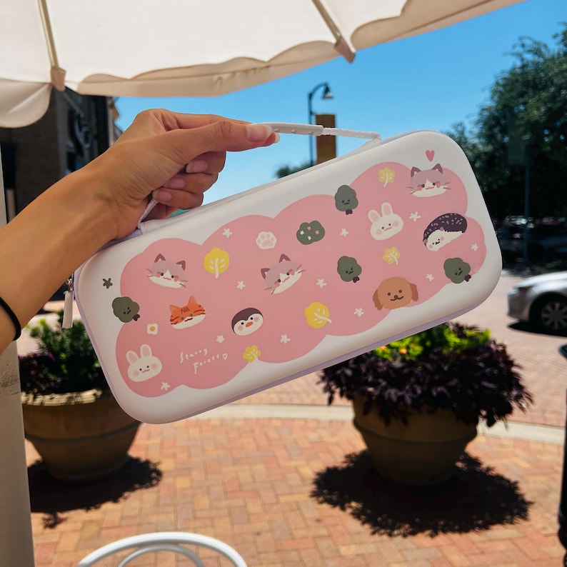 May include: White and pink carrying case with a handle, decorated with cartoon animals and trees. The case features a zipper closure and a white handle. The design includes cats, bunnies, a dog, and a hedgehog. The text "Starry Forever" is printed on the case.