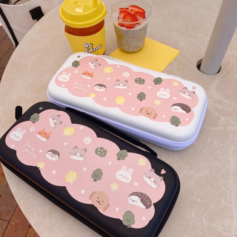 May include: Two rectangular cases, one black and one white, with a pink cloud design. The cloud design features cartoon animals, trees, and stars. The cases have a zipper closure and a handle. The cases are likely for storing small items.