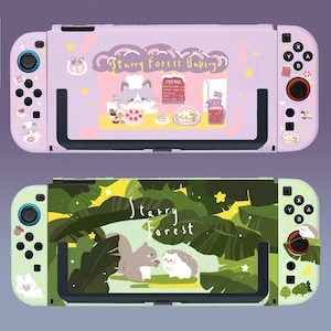 May include: Two Nintendo Switch console cases. The first case is purple with a cartoon bakery scene and the text "Starry Forest Bakery". The second case is green with a cartoon forest scene and the text "Starry Forest".