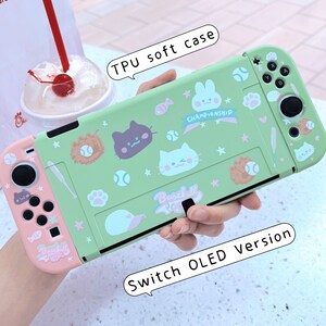 May include: A green and pink protective case for a Nintendo Switch OLED console. The case features a baseball theme with cartoon animals and the text "Baseball" and "Championship".