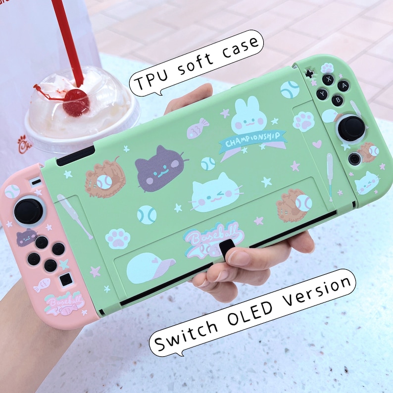 May include: A green and pink protective case for a Nintendo Switch OLED console. The case features a baseball theme with cartoon animals and the text "Baseball" and "Championship".