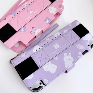 May include: Two purple and pink Nintendo Switch game cases with a cute cartoon design. The cases feature a starry sky theme with clouds, stars, and animals. The text on the cases reads "Starry Forest".