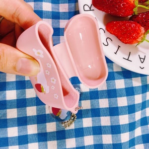 Puede incluir: Una funda de silicona rosa con dise&ntilde;o de fresa y flores para auriculares inal&aacute;mbricos. La funda tiene un peque&ntilde;o llavero.