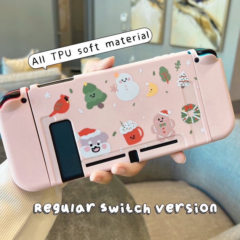 K&ouml;nnte beinhalten: Rosa Nintendo Switch H&uuml;lle mit Winter-Weihnachts-Motiv. Die H&uuml;lle zeigt einen Schneemann, einen Lebkuchenmann und andere festliche Designs. Der Text "All TPU soft material" und "Regular Switch version" ist auf der H&uuml;lle aufgedruckt.