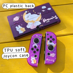May include: Purple Nintendo Switch console and Joy-Con controllers with a cute cartoon design featuring a bear sleeping on a moon, clouds, and stars. The text "Dreaming" is on the console and controllers. The console is labeled "PC plastic back" and the controllers are labeled "TPU soft Joycon case".