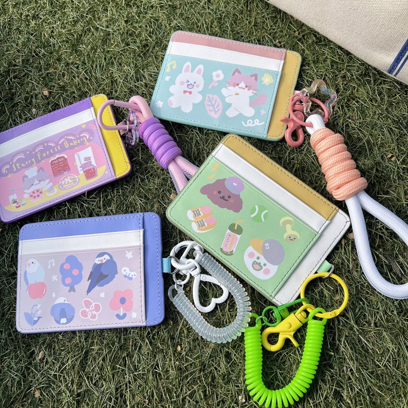 May include: Four colorful card holders with different animal illustrations and text. The card holders are attached to a white and pink coiled keychain with a silver clasp.