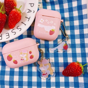 Puede incluir: Dos estuches rosas para Airpods con un encanto transparente unido a cada uno. Los encantos son una paloma blanca y un corgi. Los estuches tienen un dise&ntilde;o de fresa y flores con el texto "Starry Forest".